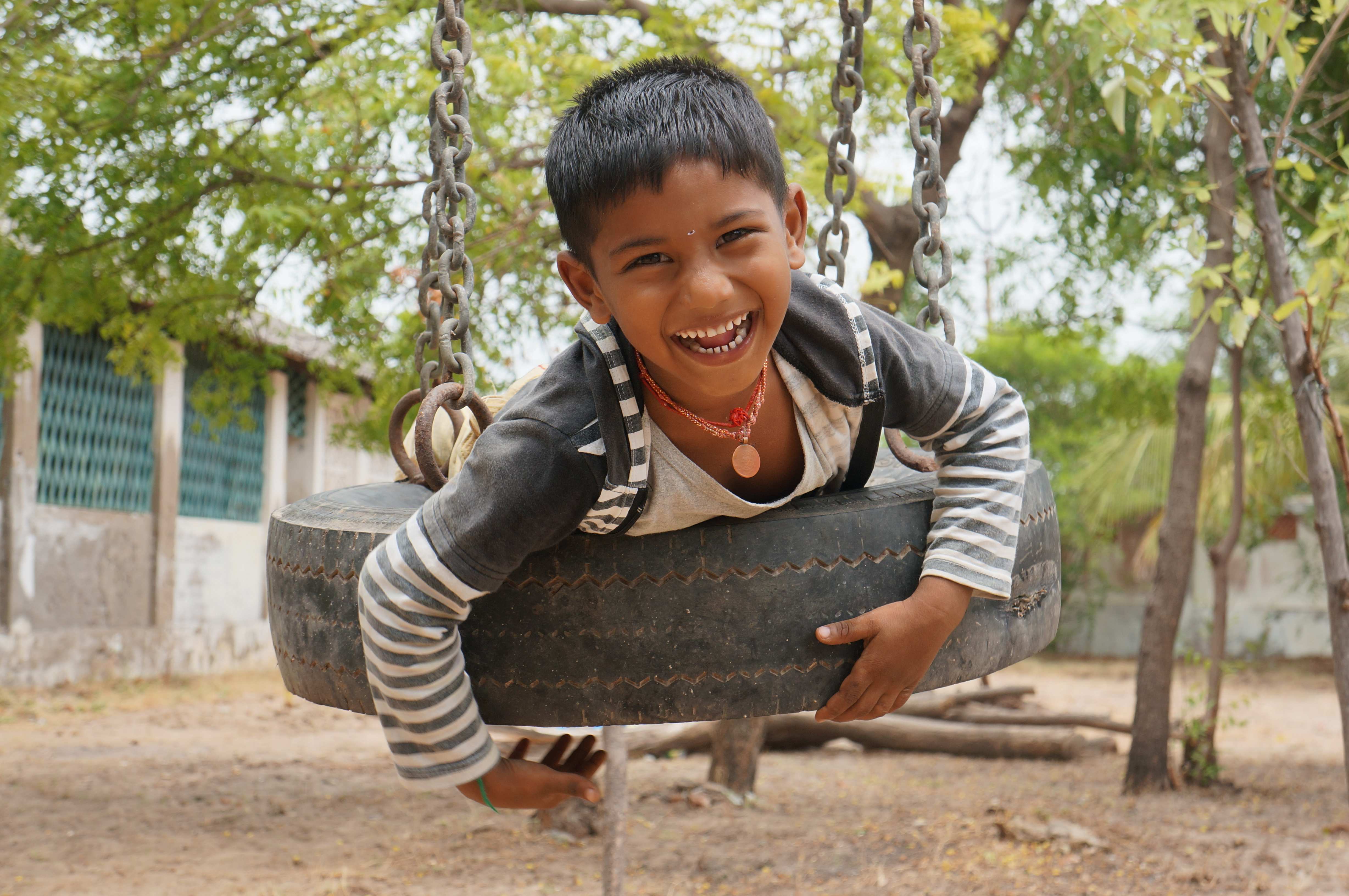 Lachender Bub auf Reifenschaukel, Südindien 